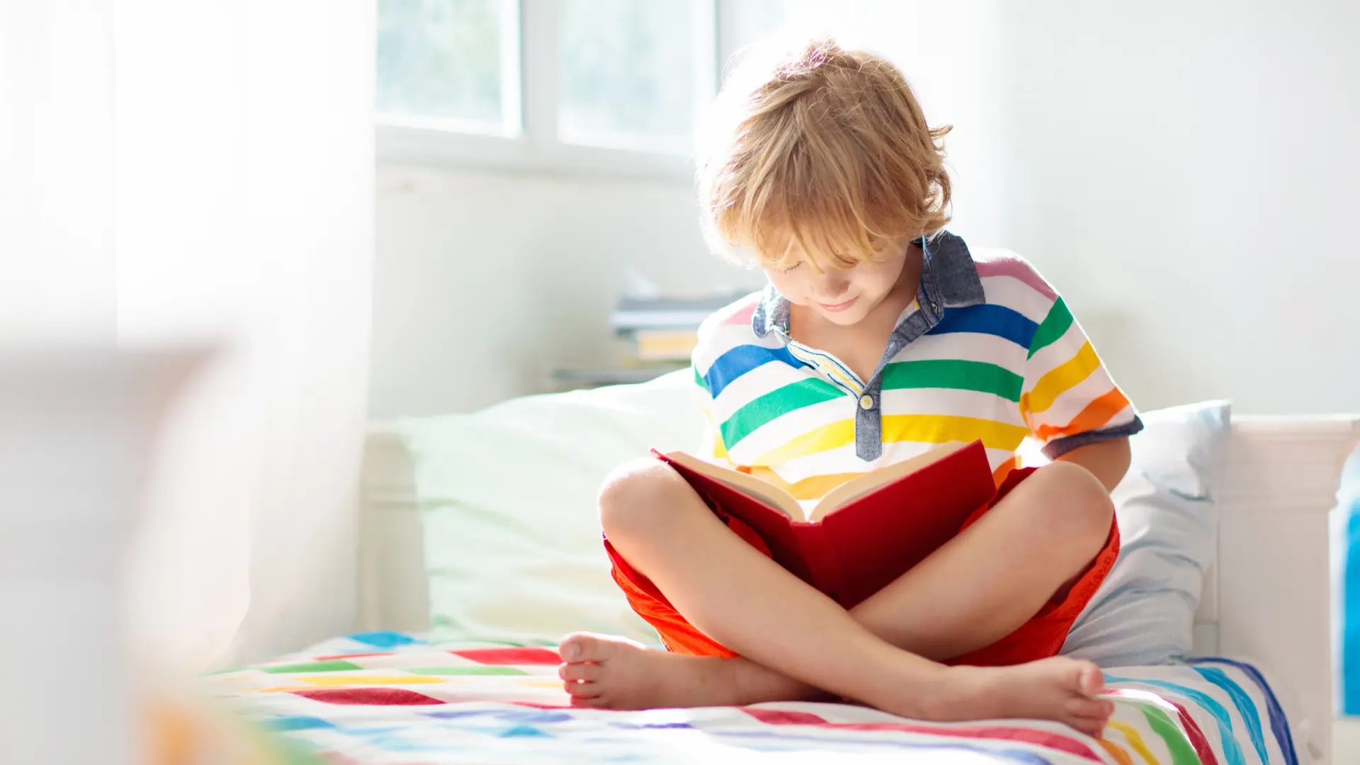 Junge in gestreiftem Hemd liest ein Buch auf seinem Bett