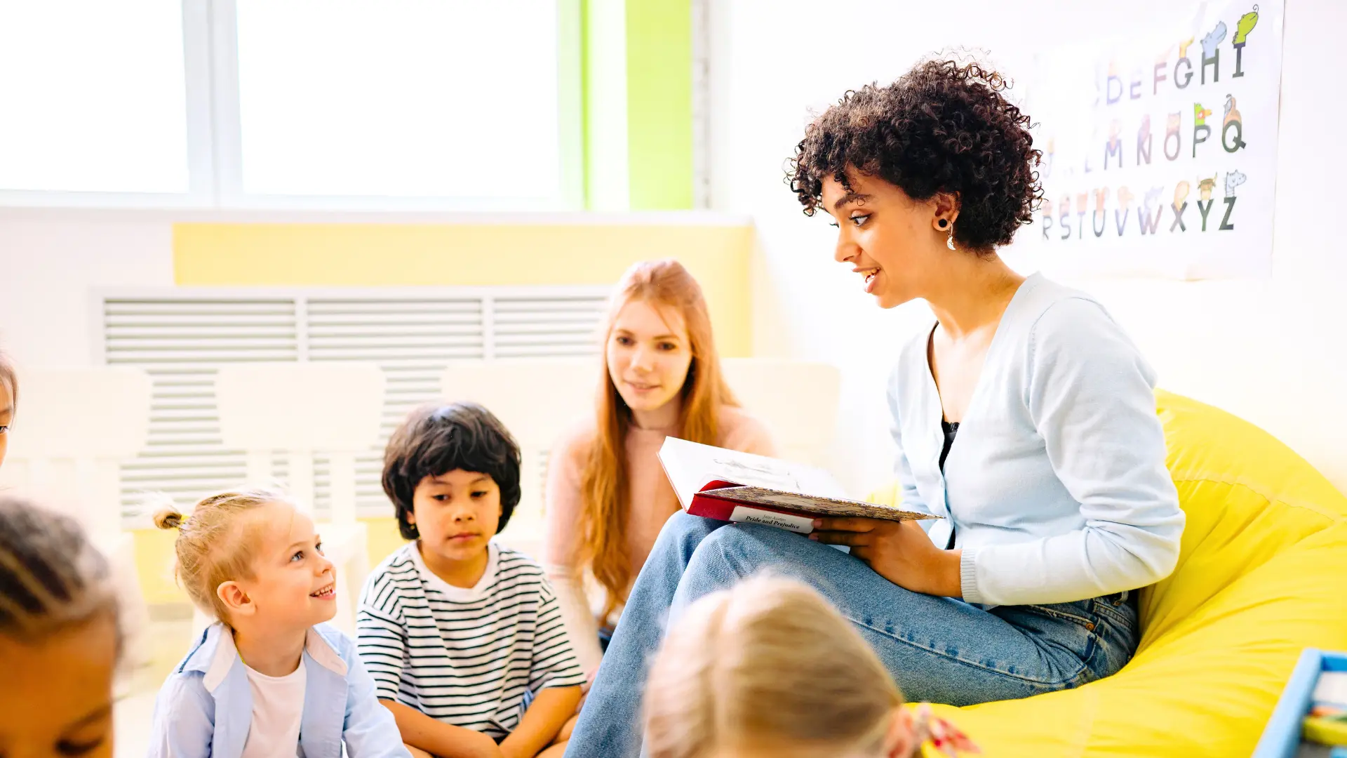 Kinder und zwei Frauen sitzen im Klassenzimmer und lesen ein Buch vor