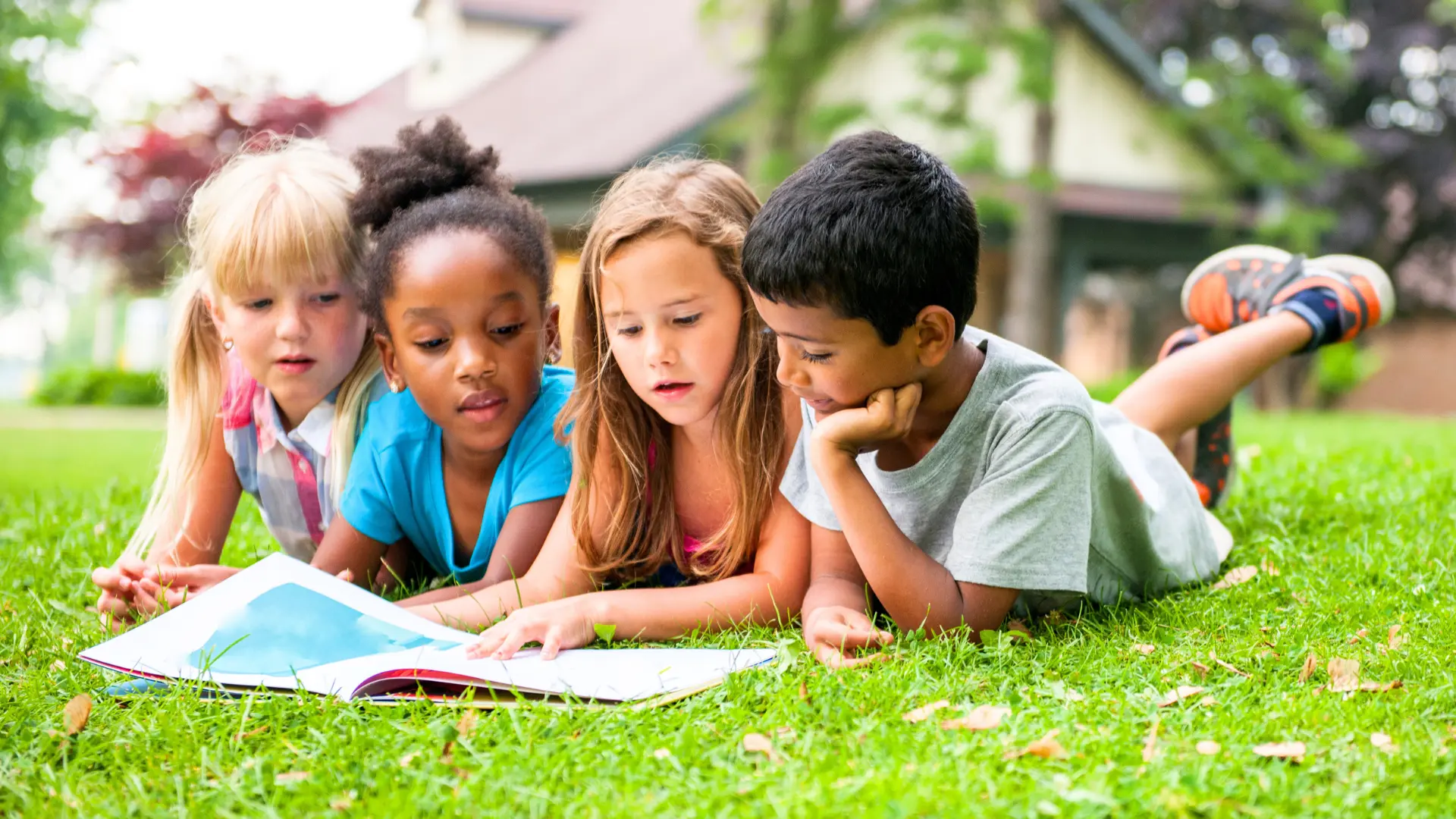 Foto von vier Kindern, die im Garten auf dem Rasen ein Buch lesen